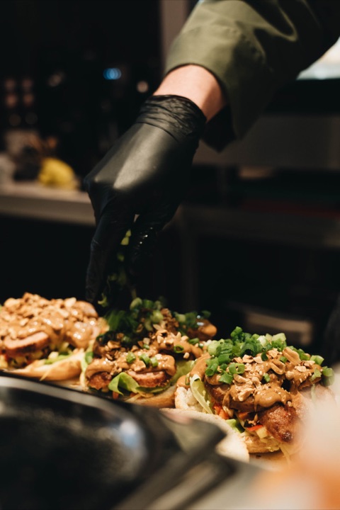 Three Indonesian meatball sandwiches being finished with lettuce, satay sauce and spring onion